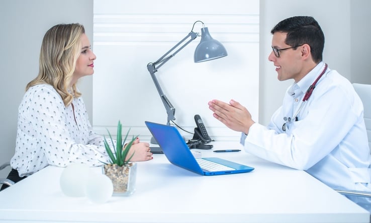 Doctor talking with a woman across a desk in a bright consultation room