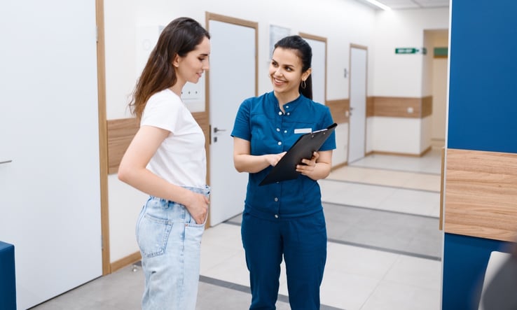 Clinician talking with a patient in a clinic hallway about symptoms after a breast biopsy